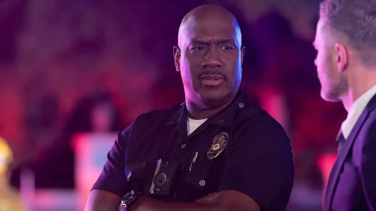 Szene aus der Serie "The Rookie"-Staffel 7: Ein männlicher Polizist schaut kritisch einen Mann im Anzug an.